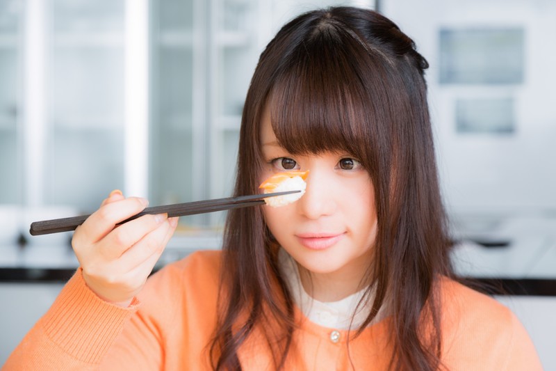 箸で寿司をつかみ見つめる女性